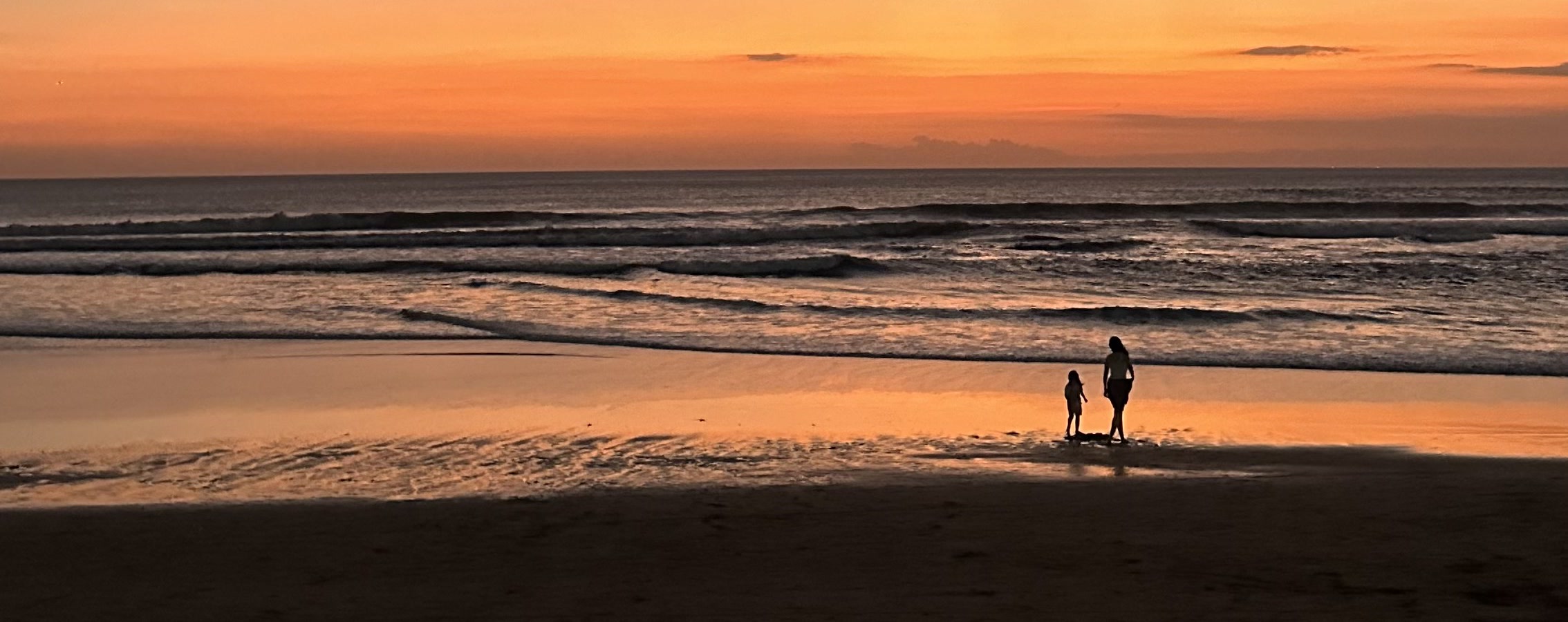 Two people standing together at the shoreline during a Bali sunset